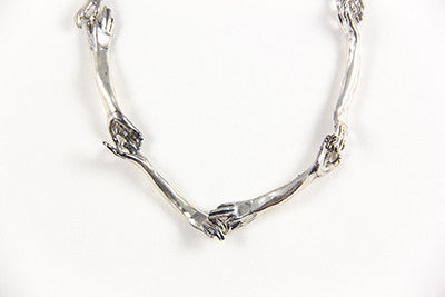 A silver necklace with a unique design featuring hand-shaped links connected by silver rings on a silver chain, by Alice Scott, on gray background.
