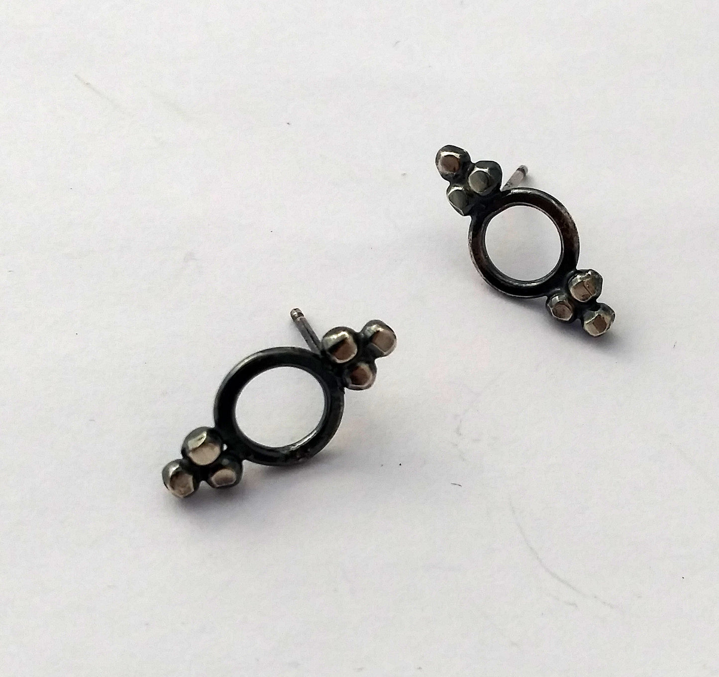 A pair of Victorian-style stud earrings with blackened sterling silver dots and circular inside, displayed on a textured surface, by Alice Scott