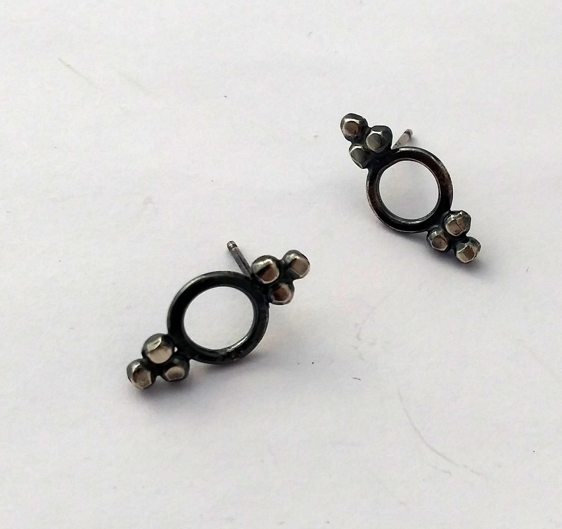 A pair of Victorian-style stud earrings with blackened sterling silver dots and circular inside, displayed on a textured surface, by Alice Scott