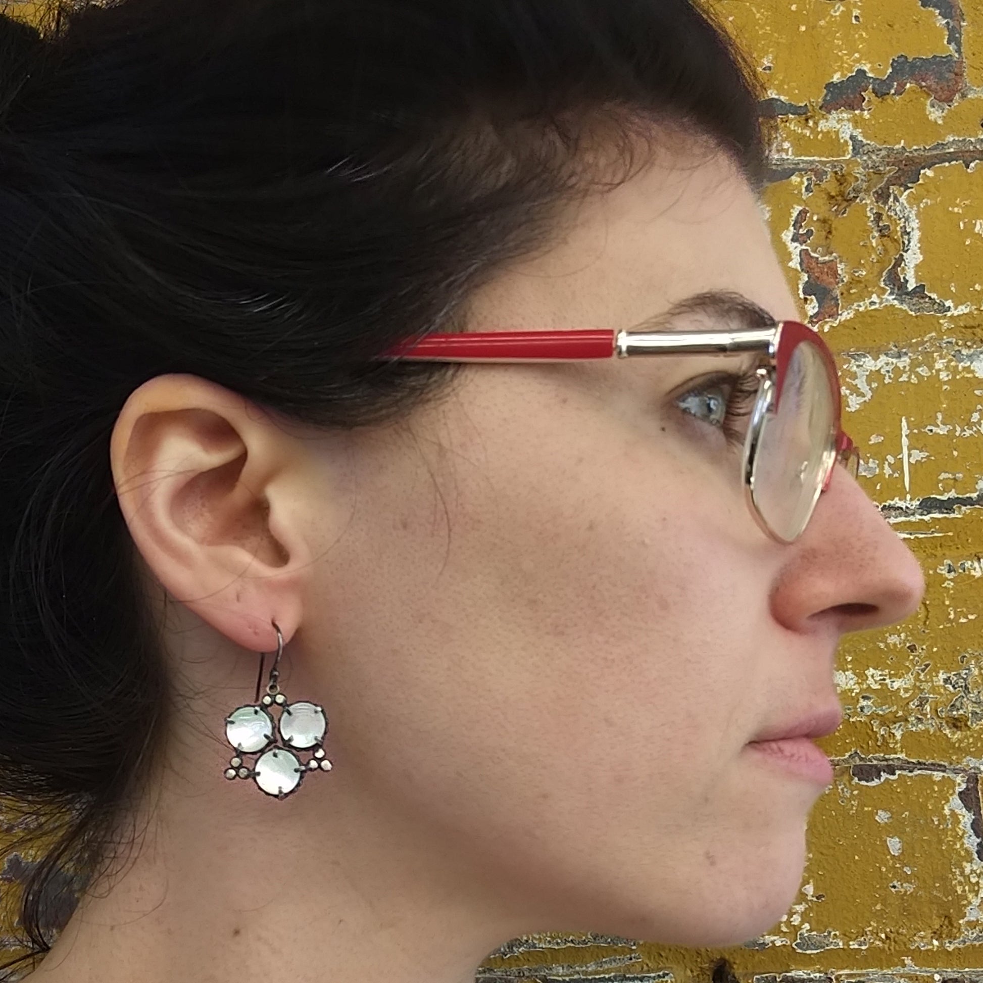 A pair of geometric pearl star earrings laid out on a model profile, showcasing circular mother of pearl stones with sterling silver accents by Alice Scott